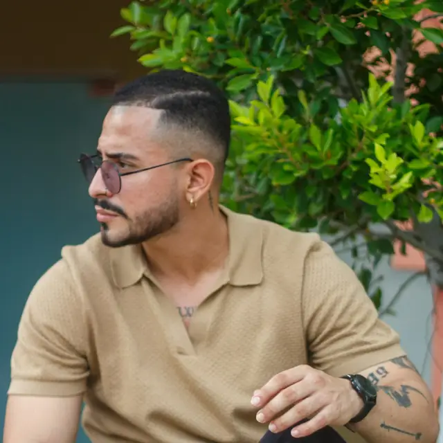 Man in a tan knit polo sitting outdoors