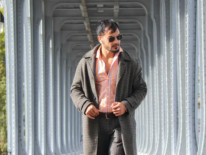 Man in a grey overcoat under a steel bridge