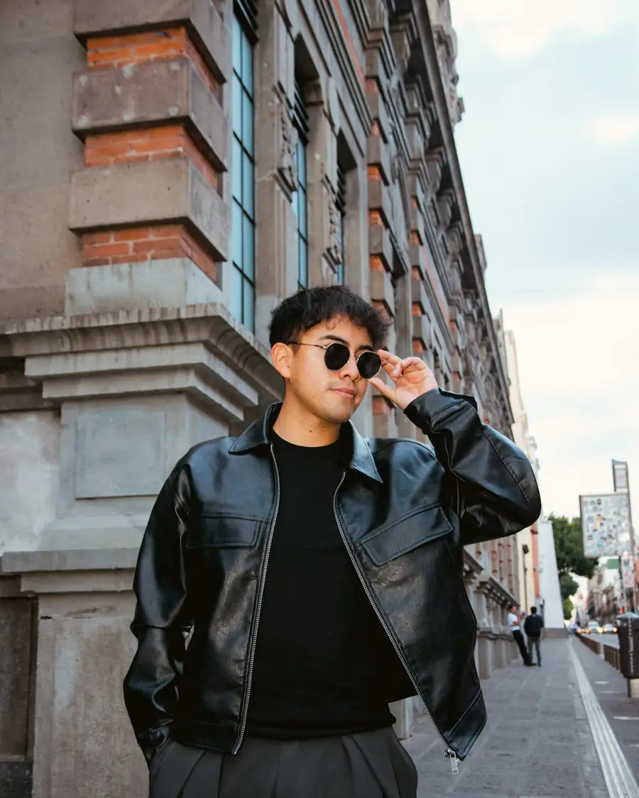 Man in a black leather jacket, black tee and charcoal trousers on a city street