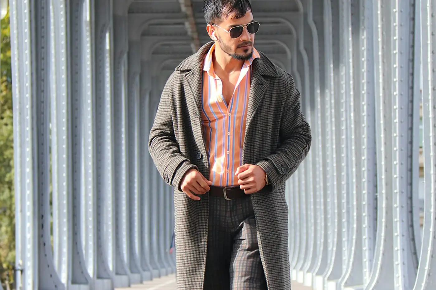 Man in a grey overcoat walking under a steel bridge